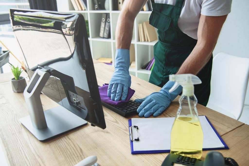 bijgesneden schot van professionele reiniger in rubberen handschoenen schoonmaken toetsenbord van de computer in kantoor - Foto, afbeelding
