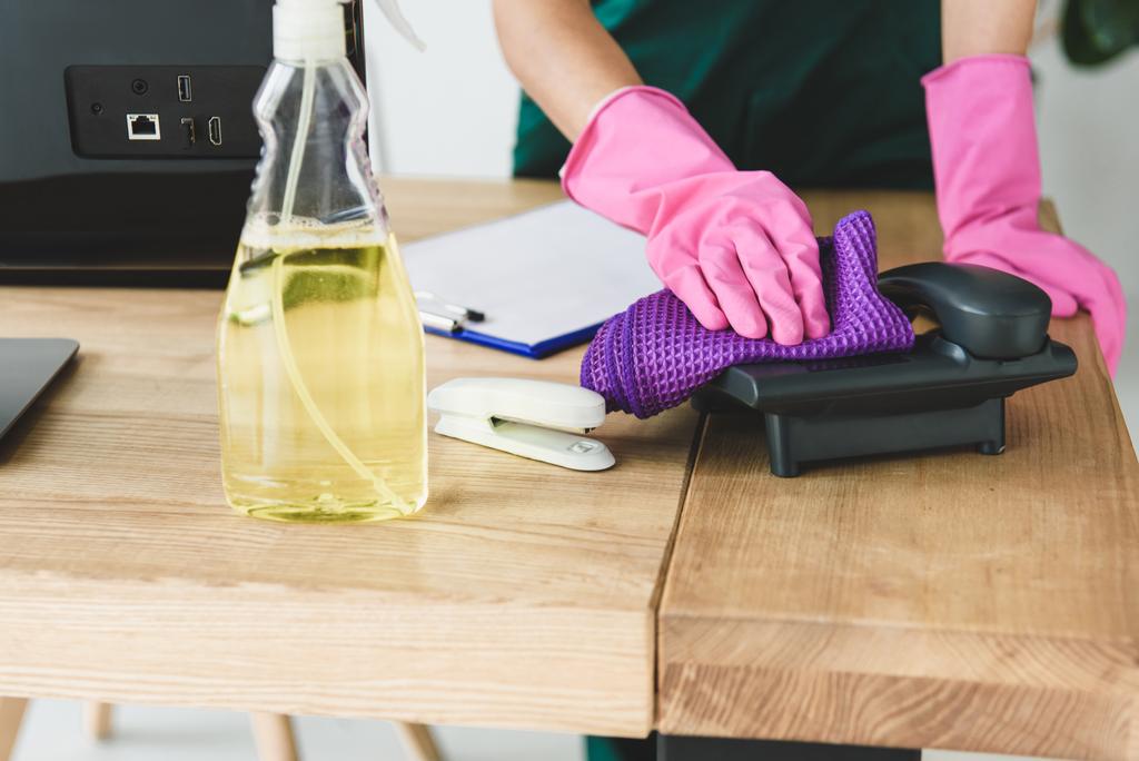 tiro recortado de la mujer en guantes de goma teléfono de limpieza en la mesa en la oficina
 - Foto, Imagen