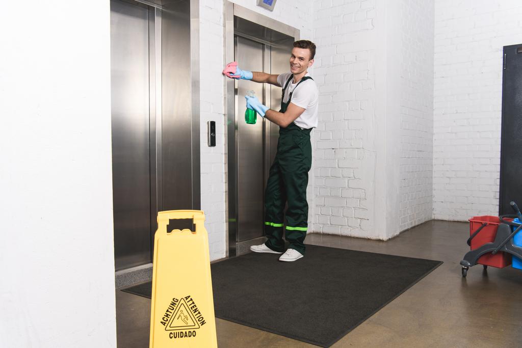schöner junger Hausmeister putzt Fahrstuhl und lächelt in die Kamera  - Foto, Bild
