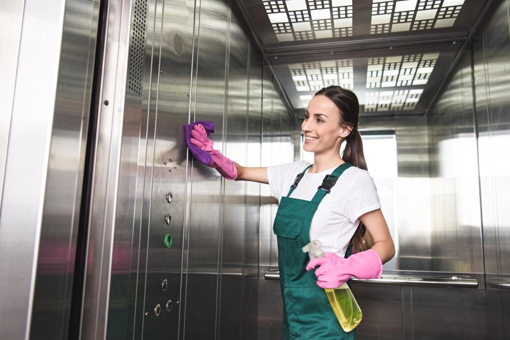 hermoso limpiador joven sonriente lavado ascensor con detergente y trapo
  - Foto, Imagen