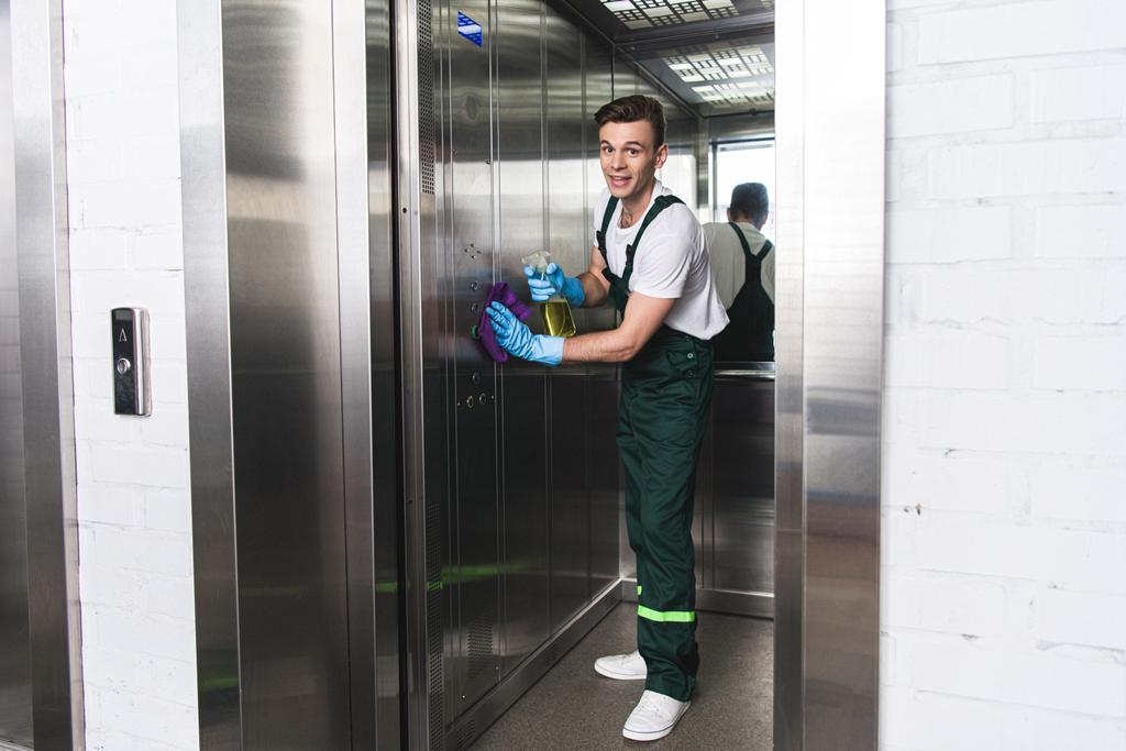 csinos, fiatal férfi takarítás a lift, és mosolyogva kamera    - Fotó, kép