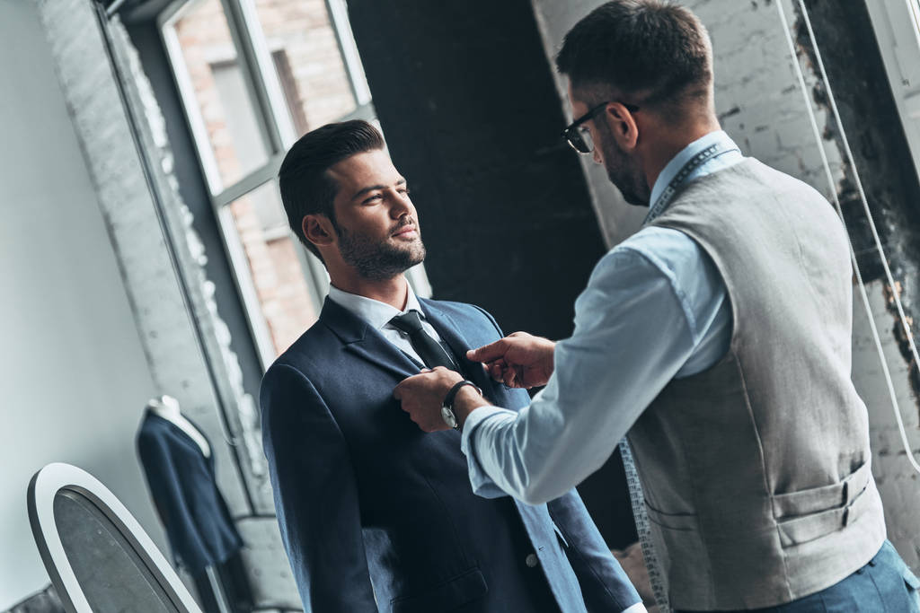 modieuze ontwerper helpen van zijn cliënt, pak jasje met stropdas aan te passen  - Foto, afbeelding