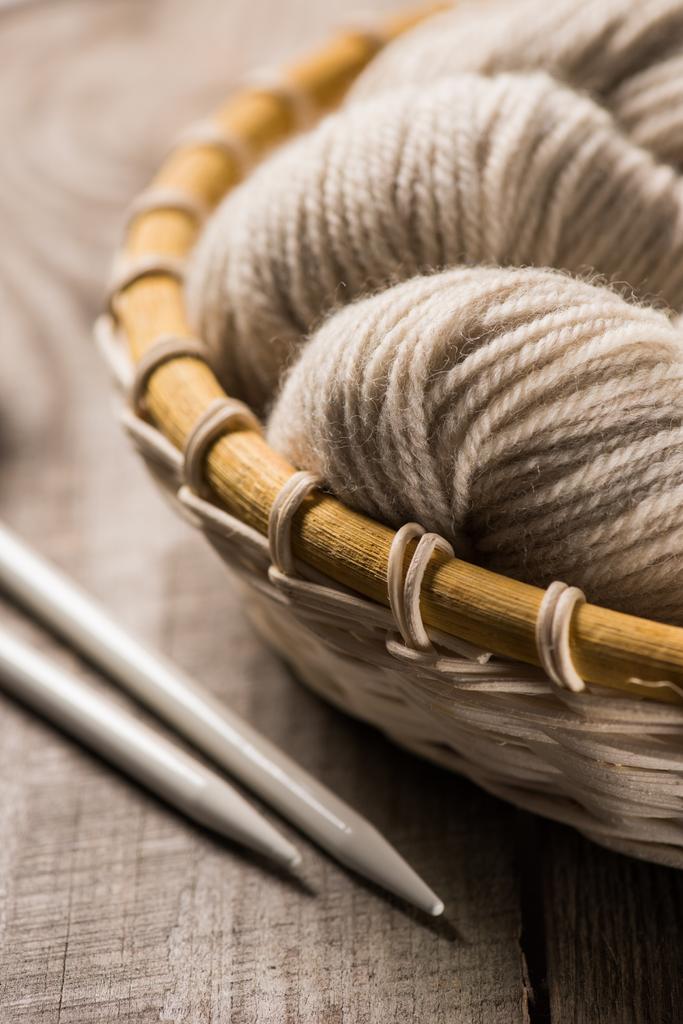 foco seletivo de fios de lã de malha bege na cesta de vime perto de agulhas de malha no fundo de madeira
  - Foto, Imagem
