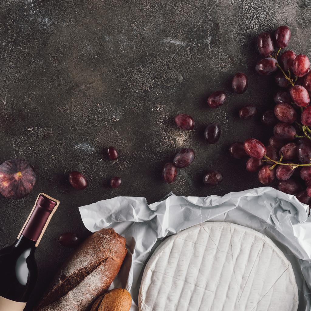 deitado plano com composição de alimentos de pão loafs, queijo camembert e garrafa de vinho na superfície escura
 - Foto, Imagem