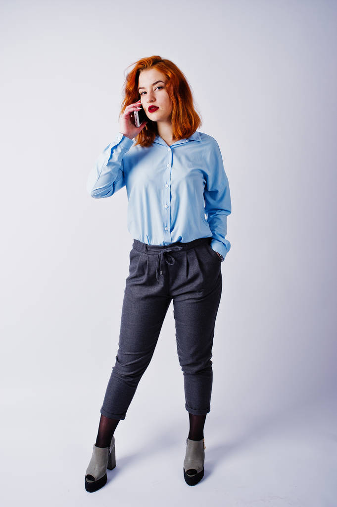 Retrato de una joven mujer de negocios pelirroja con camisa azul y pantalones hablando por teléfono
. - Foto, Imagen
