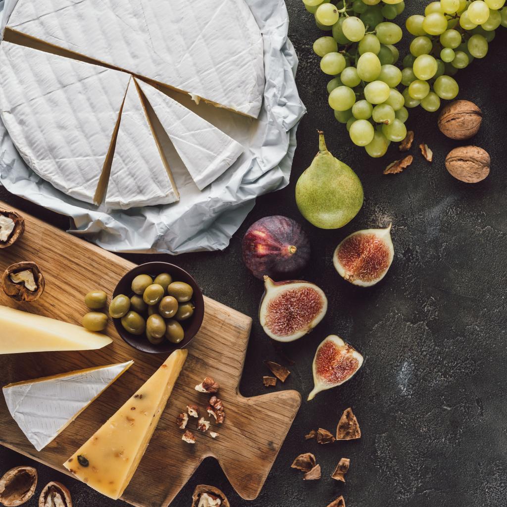 Draufsicht auf Käse, Oliven in Schale und Früchte auf dunkler Tischplatte - Foto, Bild
