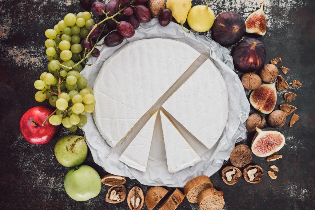 vista superior de queijo brie, avelãs e frutas dispostas na superfície escura
 - Foto, Imagem