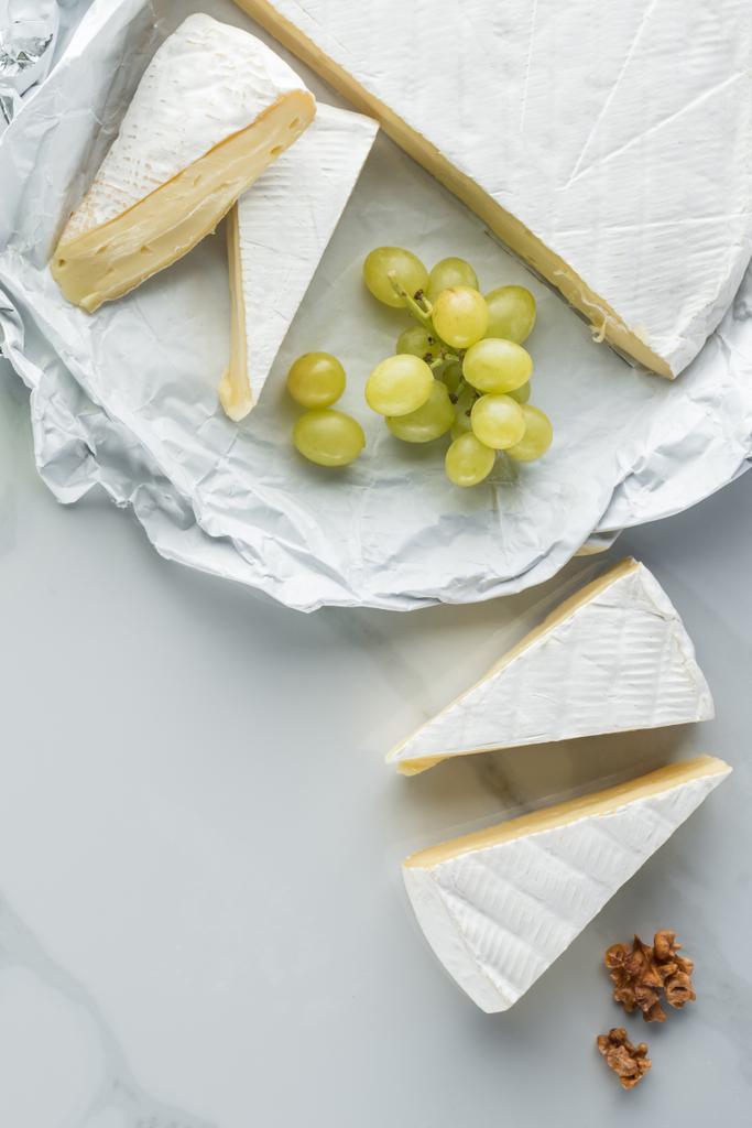 flat lay with camembert cheese, hazelnuts and grape on white marble surface - Photo, Image