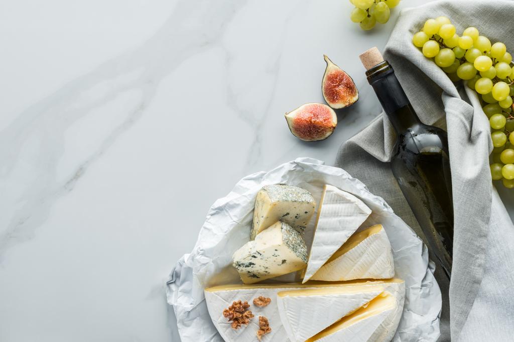 çeşitli peynir, şişe şarap ve incir adet beyaz mermer yüzeyi düz lay - Fotoğraf, Görsel