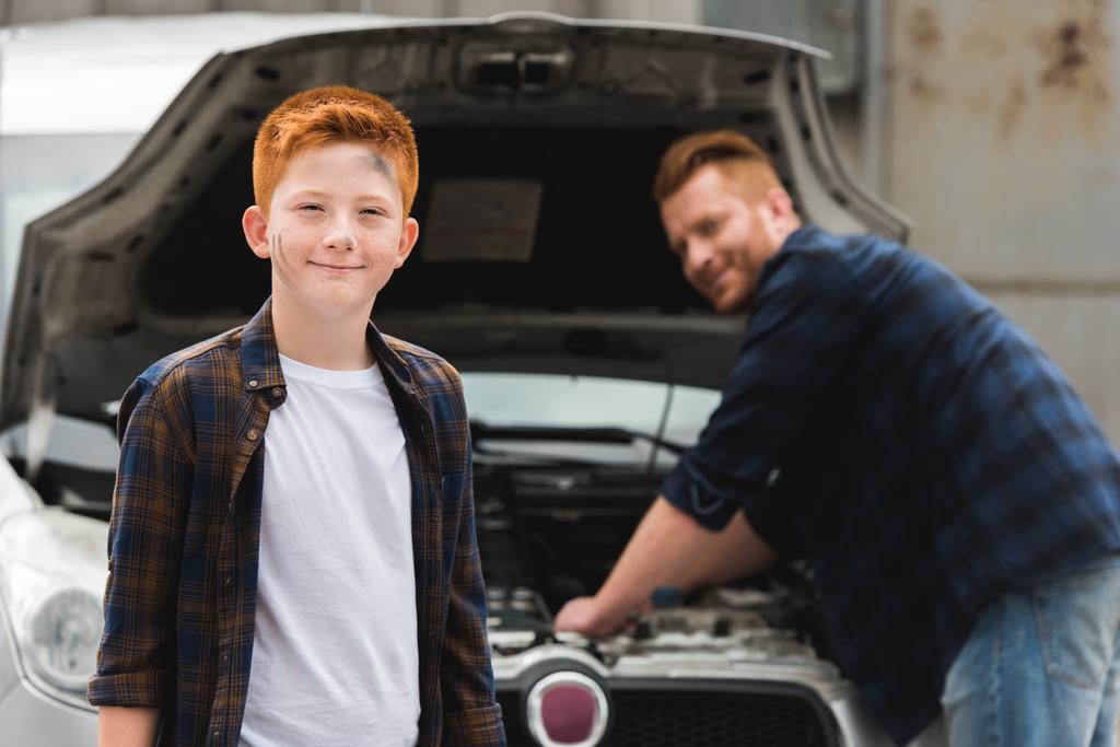 apa és javítási autó nyitott motorháztető, mosolyogva a fiú keresi a kamera - Fotó, kép