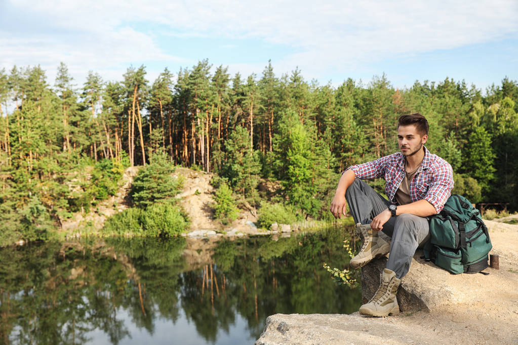 Jongeman op rots in de buurt van meer en bos. Camping seizoen - Foto, afbeelding