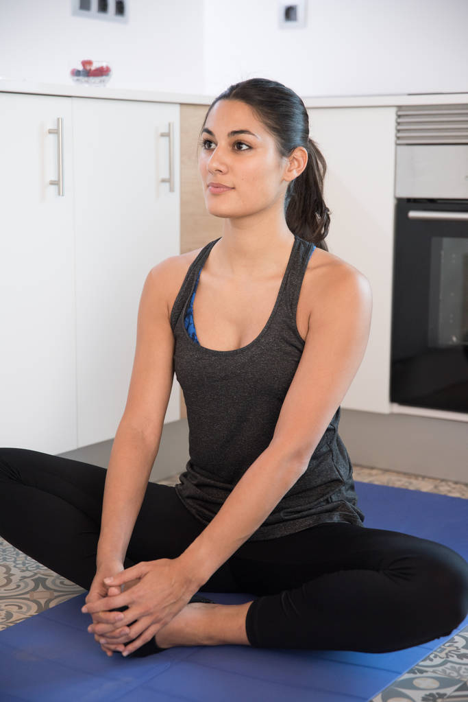 Mujer mirando hacia adelante mientras se sienta en una pose de yoga con piernas cruzadas sobre una alfombra azul
 - Foto, imagen