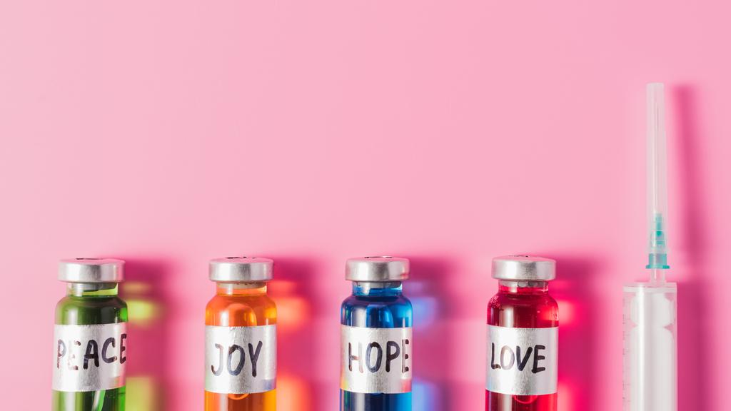 pohled shora z injekční stříkačky a lahvičky s lásky, naděje, radost a mír vakcína znaky v řádku na růžové povrchu - Fotografie, Obrázek