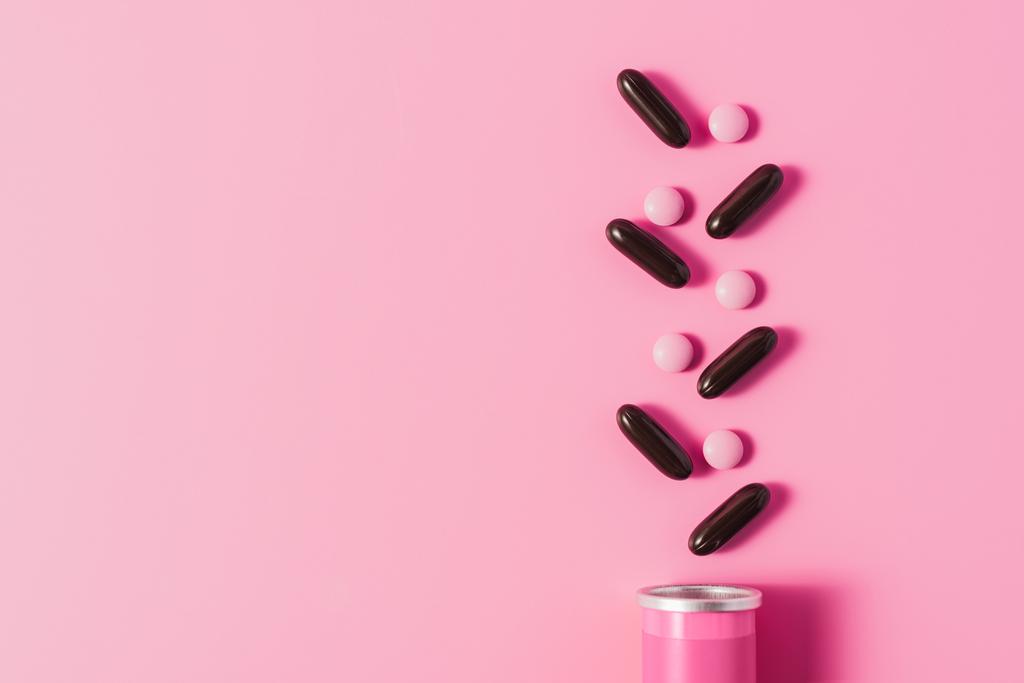 Draufsicht auf Dose mit rosa und schwarzen Pillen auf rosa - Foto, Bild