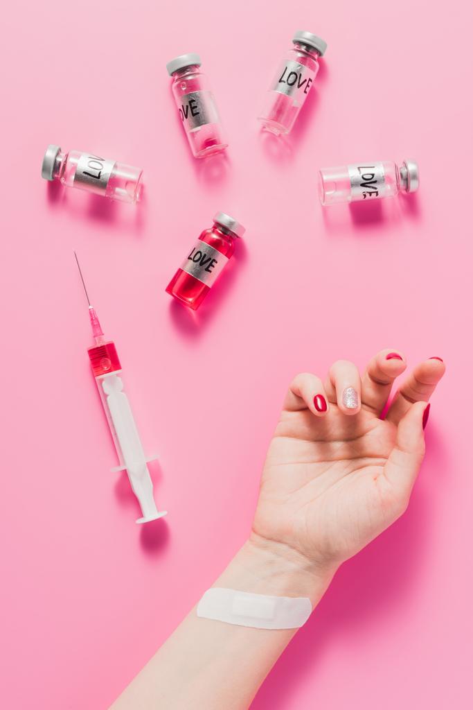 Colpo ritagliato di mano femminile sdraiata sulla superficie rosa con siringa e flaconi con segni di vaccino d'amore
 - Foto, immagini