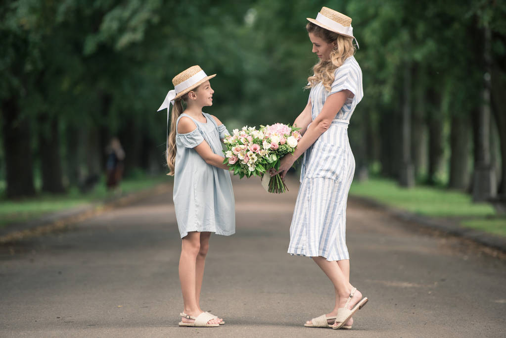 ママと娘が公園で手をつないでの花の花束と麦わら帽子 - 写真・画像