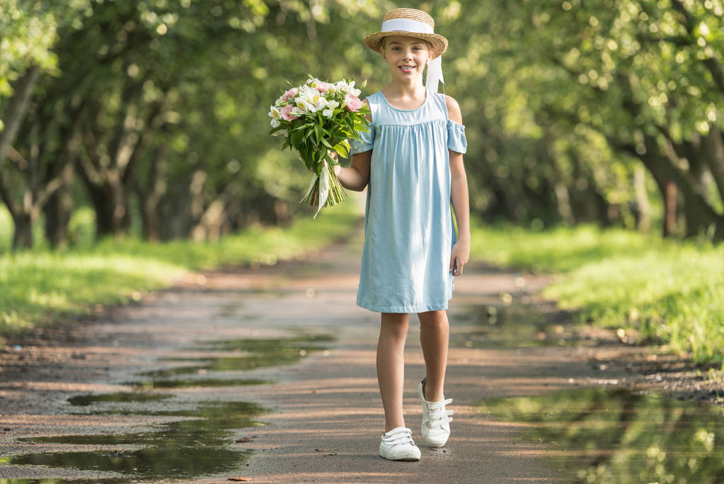 élégant enfant préadolescent en robe à la mode et chapeau de paille tenant bouquet de fleurs
 - Photo, image