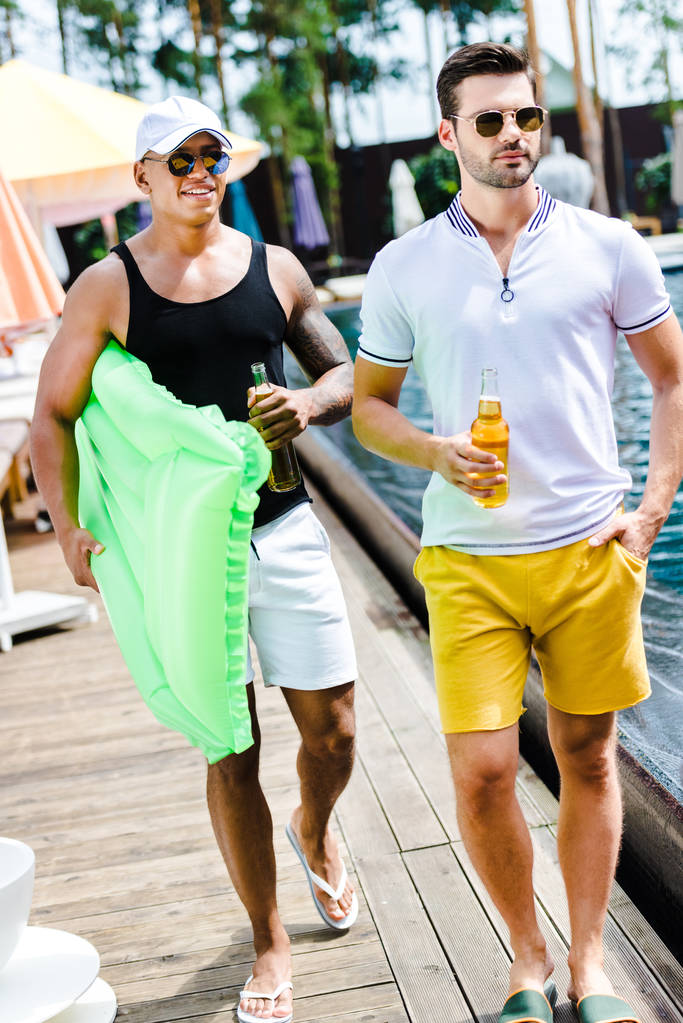 handsome male friends walking with inflatable mattress and beer near swimming pool - Photo, Image
