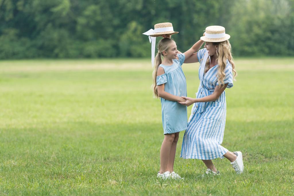 stylish mother and daughter holding straw hats over heads of each other - Photo, Image