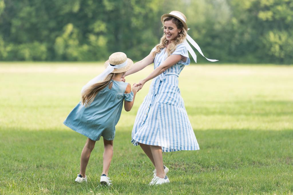 beautiful mother and daughter holding hands, twisting and having fun on green grass  - Photo, Image