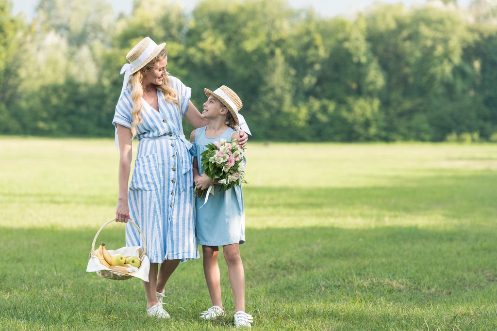 美しい母と娘は籐のバスケットと緑の芝生の上を歩いての花束 - 写真・画像