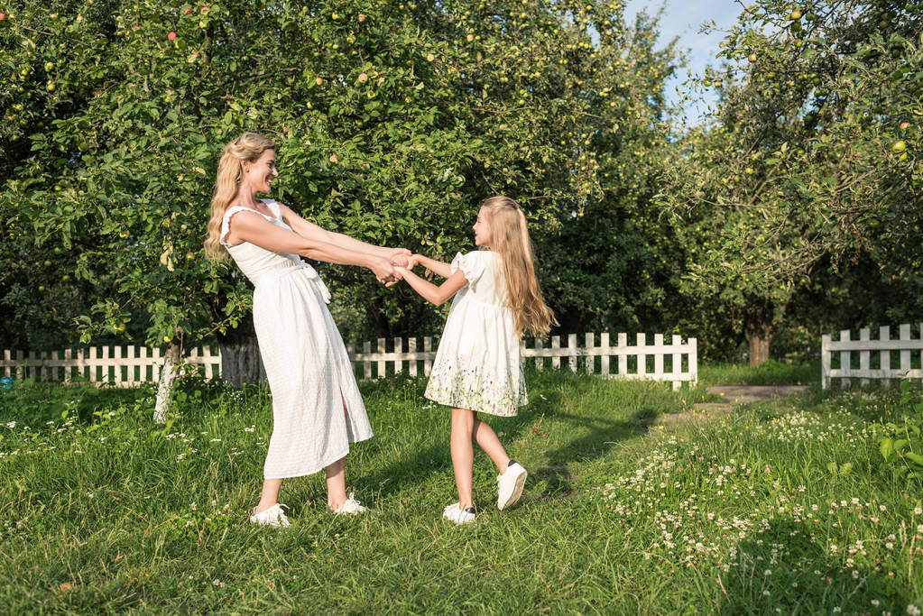 美しい母と娘の手を繋いでいると白いフェンスで庭でねじれ - 写真・画像
