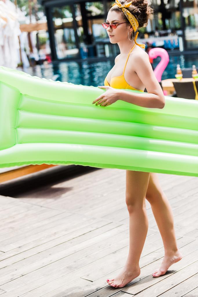 attraente ragazza in costume da bagno giallo a piedi con materasso gonfiabile vicino alla piscina
 - Foto, immagini