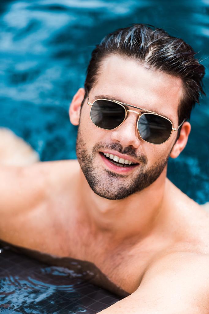 przystojny człowiek uśmiechający się w okulary, patrząc na kamery w pobliżu przy basenie - Zdjęcie, obraz