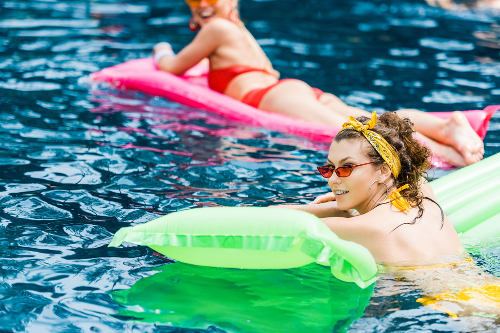 two attractive smiling women in swimsuits resting on inflatable mattresses in pool  - Photo, Image