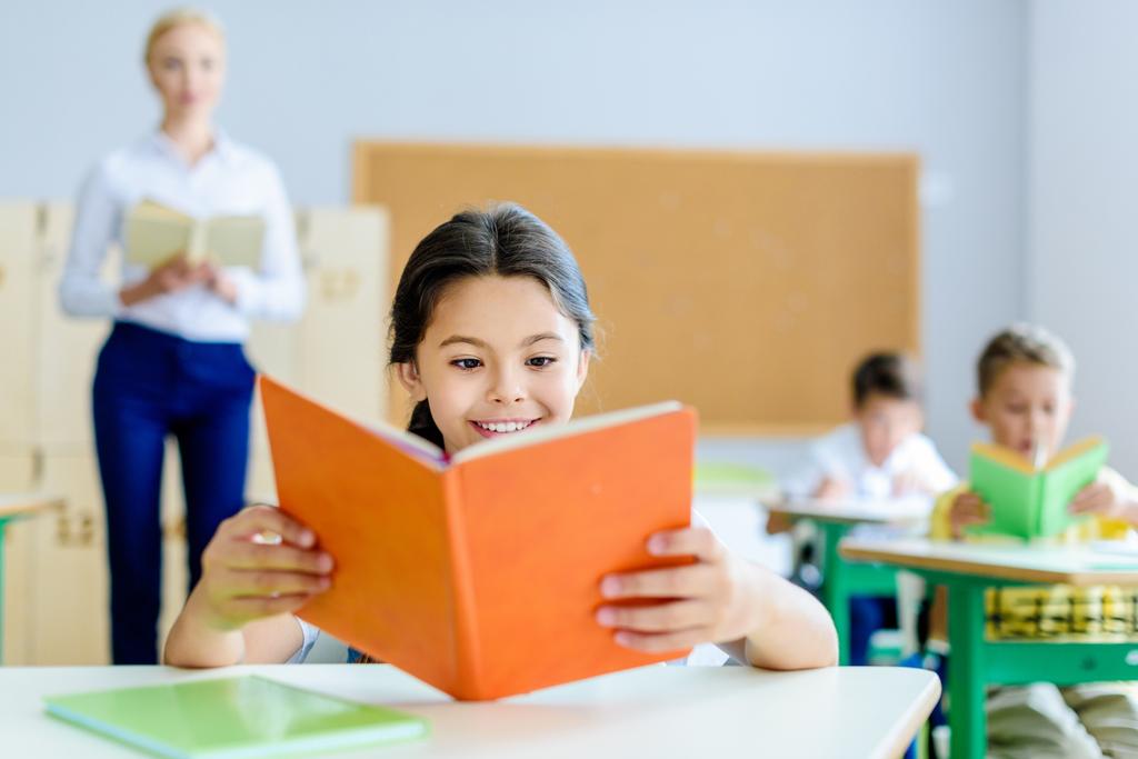 krásný usměvavý školačka čtení knih v učebně během lekce - Fotografie, Obrázek