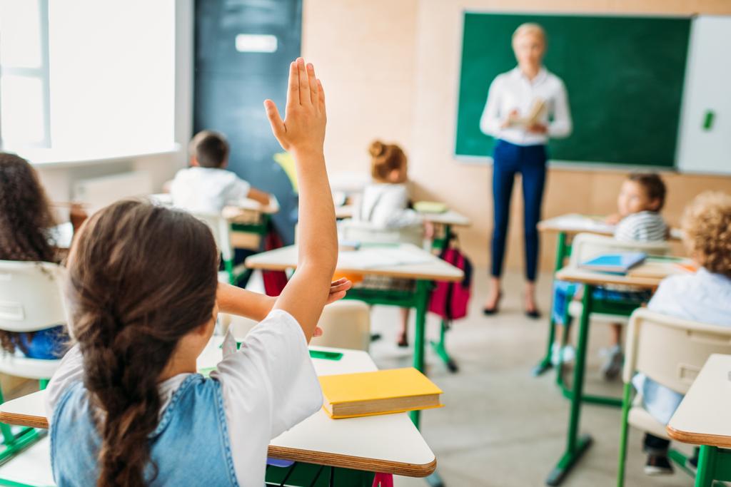 Задний вид школьницы, поднимающей руку, чтобы ответить на вопрос учителя во время урока
 - Фото, изображение