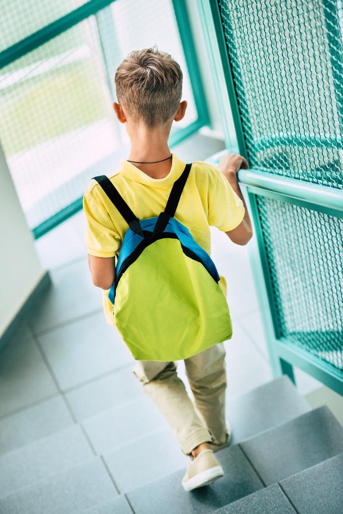 rear view of schoolboy with backpack going downstairs at school corridor - Photo, Image