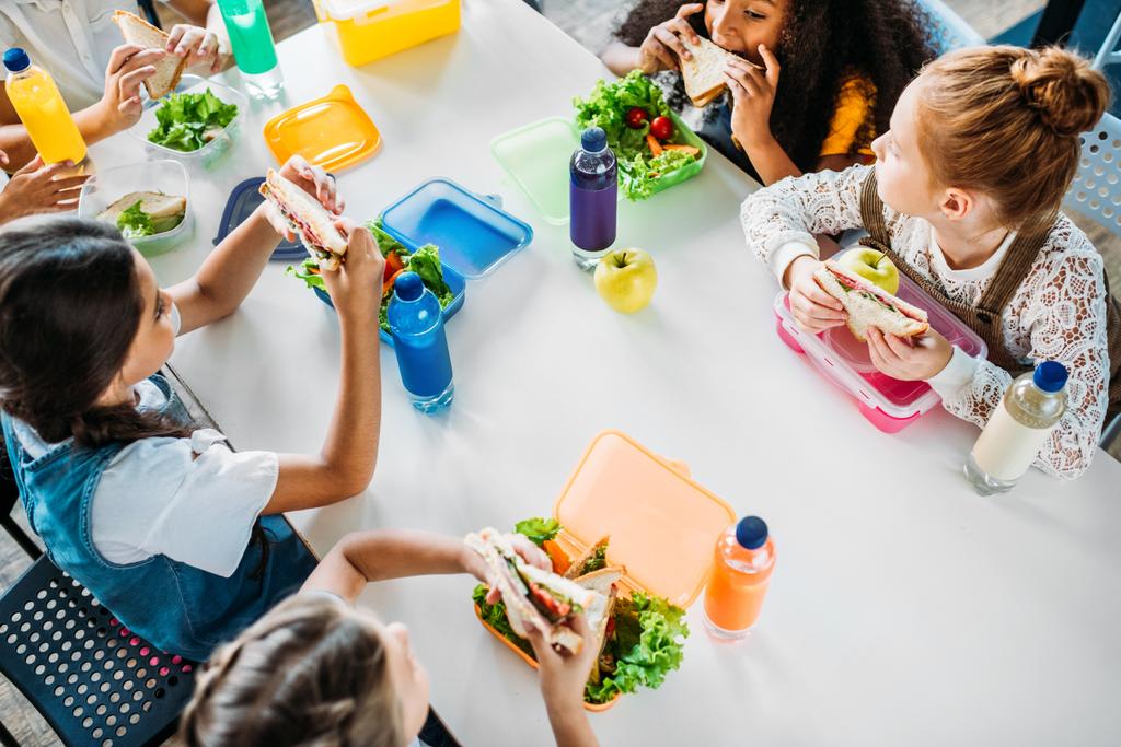 hoge hoekmening van groep schoolmeisjes nemen lunch op Schoolcafetaria - Foto, afbeelding
