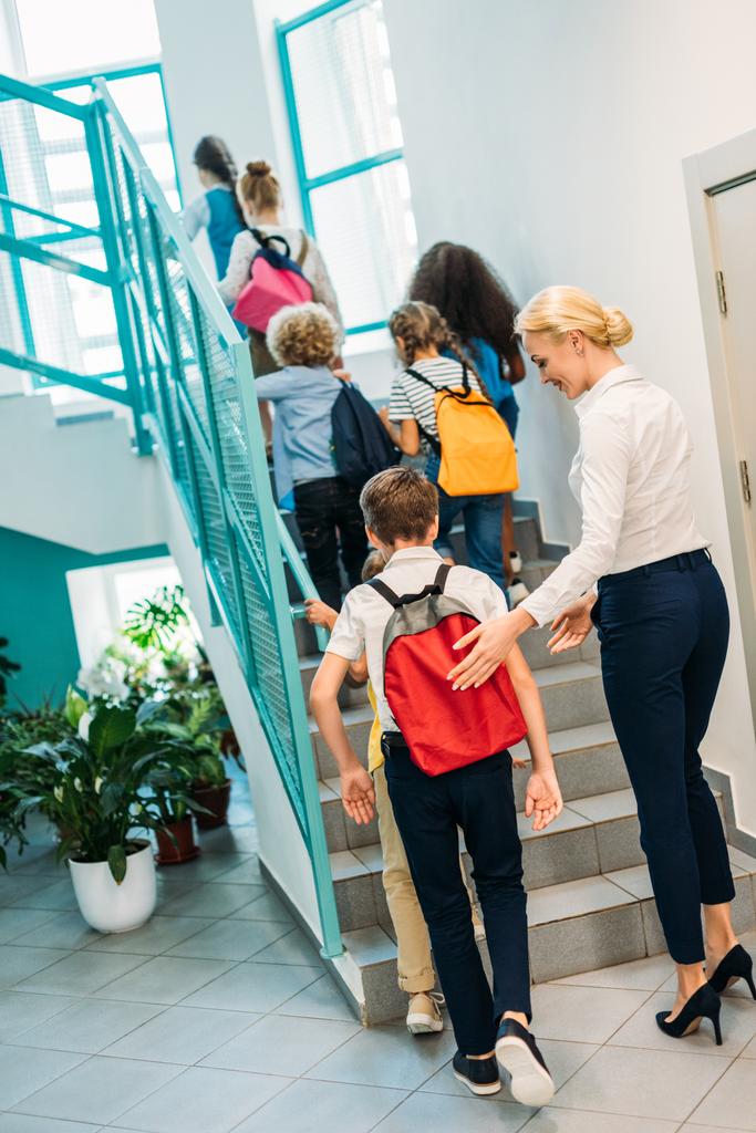 visão traseira do grupo de alunos e professor caminhando no andar de cima no corredor da escola
 - Foto, Imagem