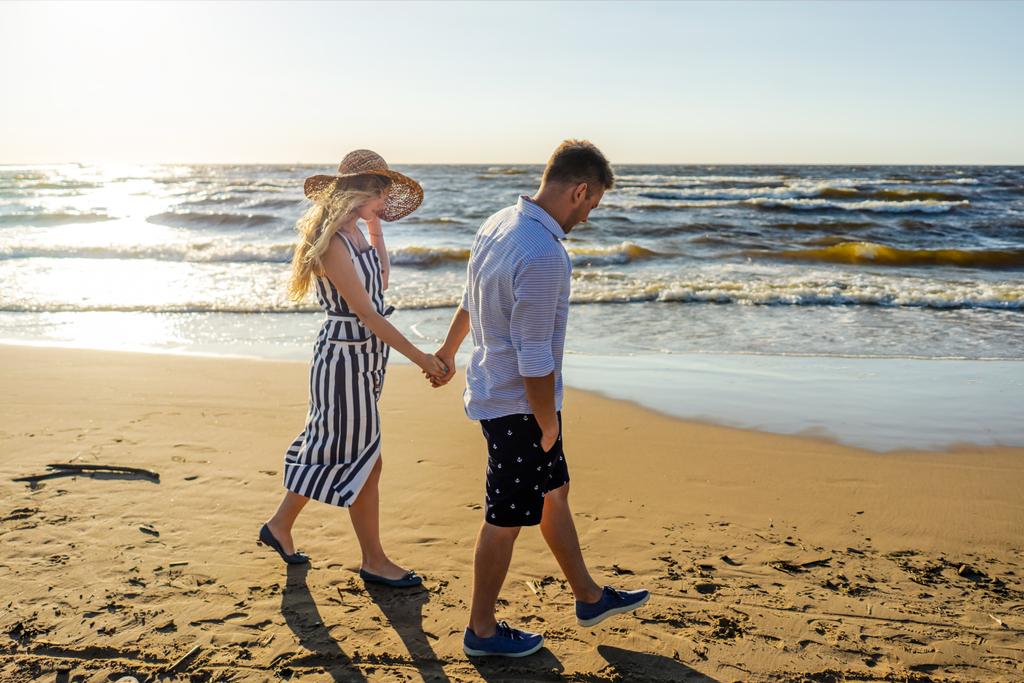 boční pohled na mladý pár v lásce, drželi se za ruce při chůzi na písečné pláži v Rize, Lotyšsko - Fotografie, Obrázek