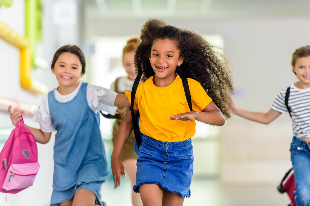 прелестные счастливые школьники, бегущие по школьному коридору вместе
 - Фото, изображение