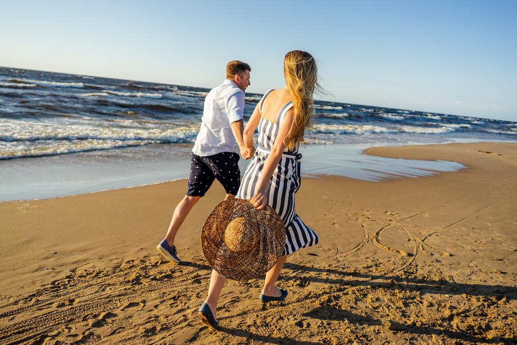 vue partielle d'un jeune couple amoureux se tenant la main et courant sur une plage de sable fin à Riga, Lettonie
 - Photo, image