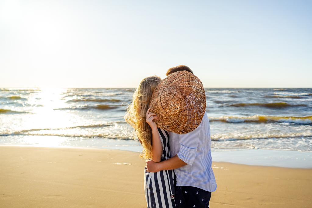 Riga, ラトビアの砂浜で麦わら帽子の後ろに隠れて愛のカップルの部分的なビュー - 写真・画像