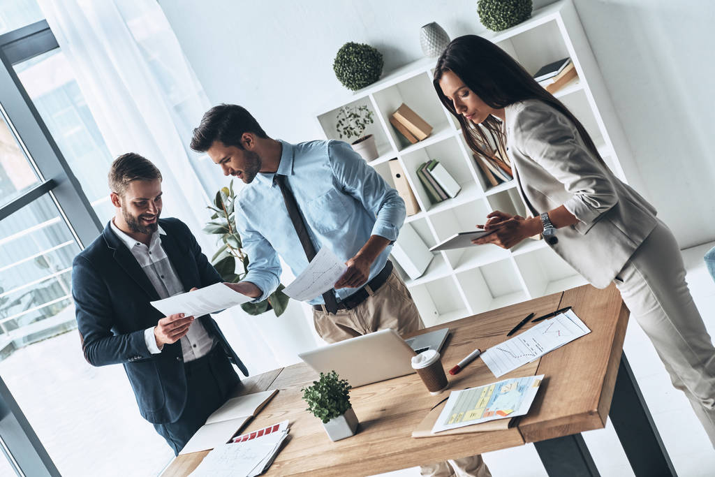 современные люди обсуждают бизнес, стоя в творческом офисе с бумагами
                - Фото, изображение
