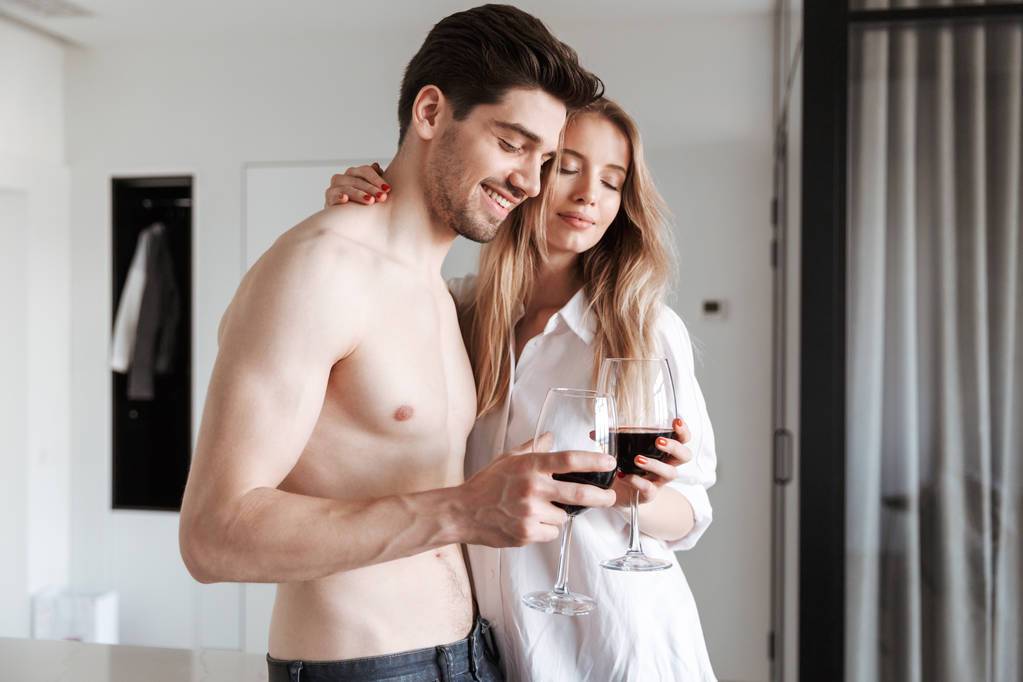 Foto de joven linda pareja amorosa feliz en casa en interiores bebiendo vino
. - Foto, imagen