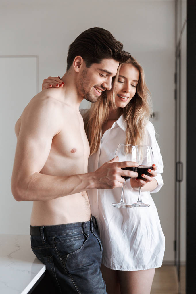 Imagen de joven linda y alegre pareja amorosa en casa en interiores bebiendo vino
. - Foto, Imagen