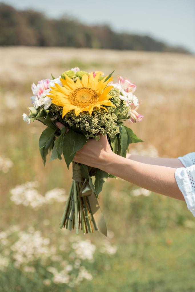 обрезанный снимок женщины, держащей букет диких цветов в поле
 - Фото, изображение