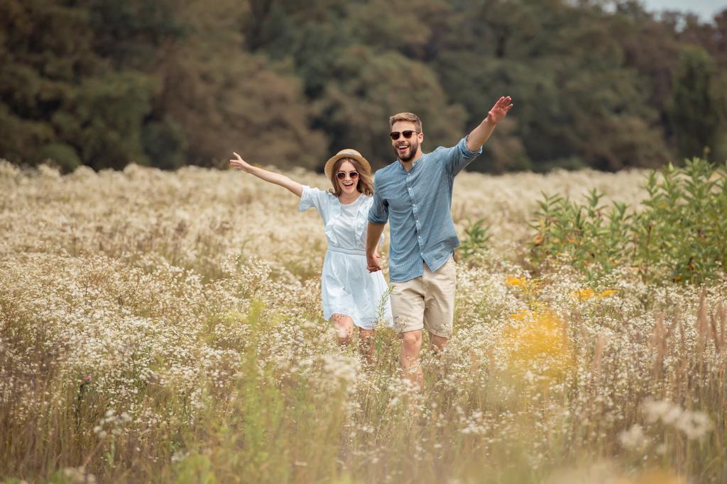 щасливі коханці тримаються за руки під час бігу в полі з дикими квітами
 - Фото, зображення