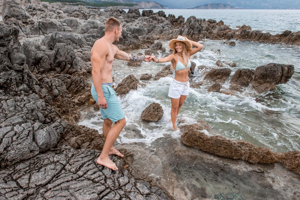 heureux jeune couple se tenant la main et se souriant sur la plage rocheuse à montenegro
 - Photo, image