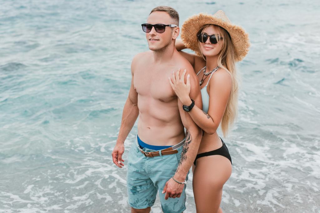 όμορφη happy νεαρό ζευγάρι σε γυαλιά ηλίου στέκεται μαζί στην πανέμορφη παραλία του Μαυροβουνίου - Φωτογραφία, εικόνα