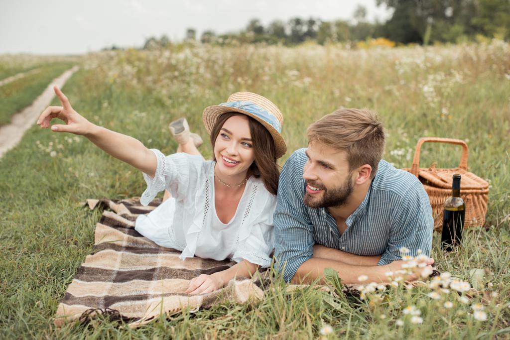 donna sorridente che mostra qualcosa al fidanzato mentre riposa sulla coperta insieme nel campo estivo
 - Foto, immagini