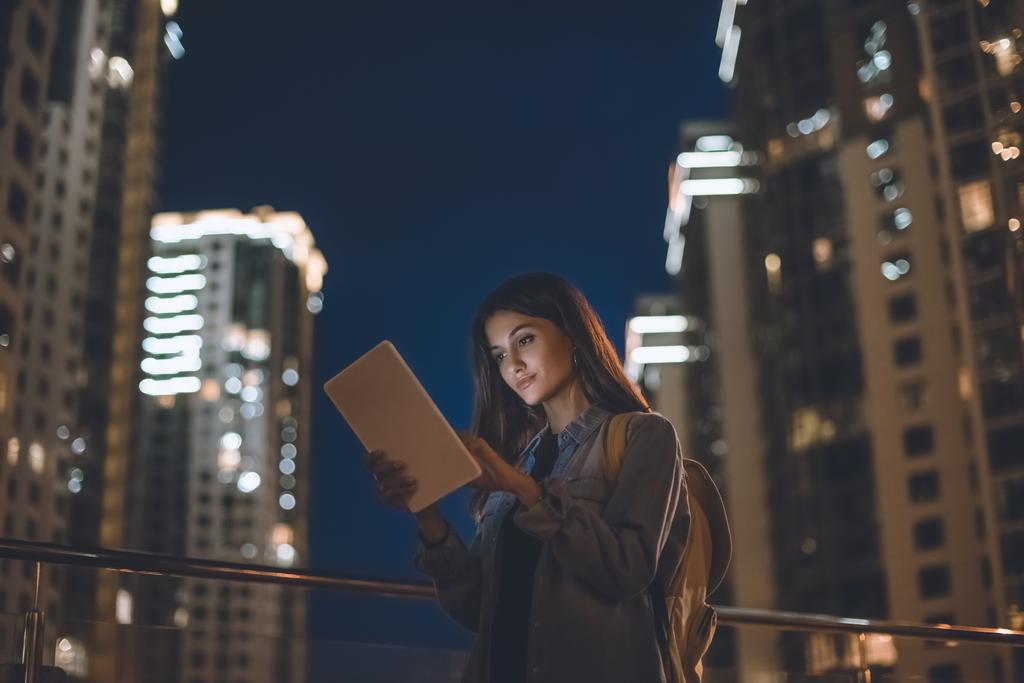puolella näkymä houkutteleva nainen käyttää digitaalista tabletti kaupungin kadulla yöllä
 - Valokuva, kuva
