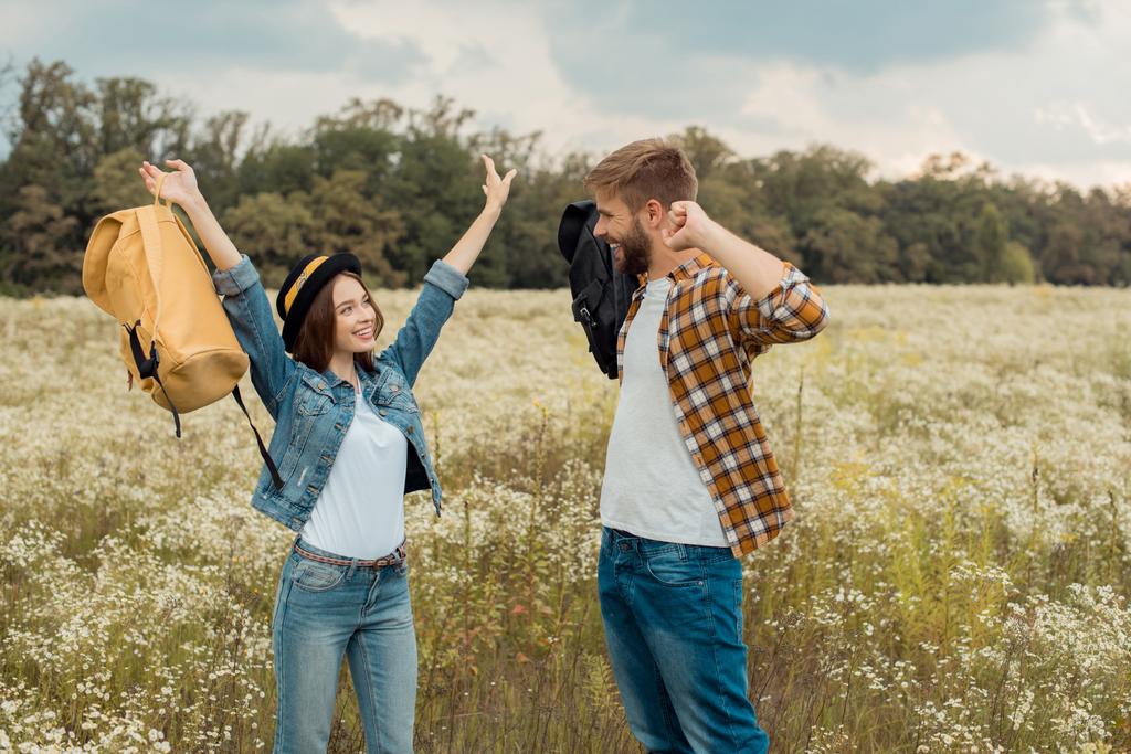 cheerful couple with backpacks in summer field with wild flowers - Photo, Image