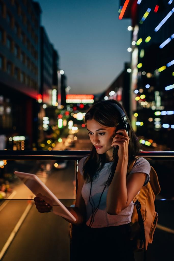 portrait of woman in headphones using tablet on street with night city lights on background - Photo, Image
