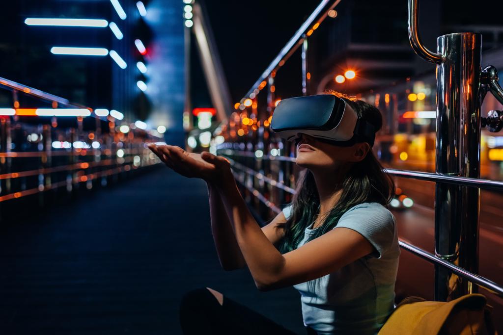 Młoda kobieta siedzi na ulicy z miasta noc na tle zestaw wirtualnej rzeczywistości - Zdjęcie, obraz